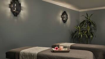 Una stanza spa con due lettini per massaggi, un vassoio con candele e una pianta in vaso.