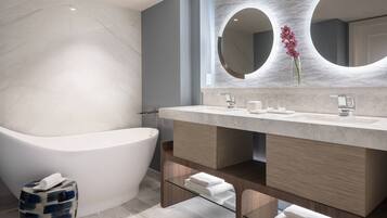 A modern bathroom with a freestanding bathtub, a large mirror, and a marble wall.