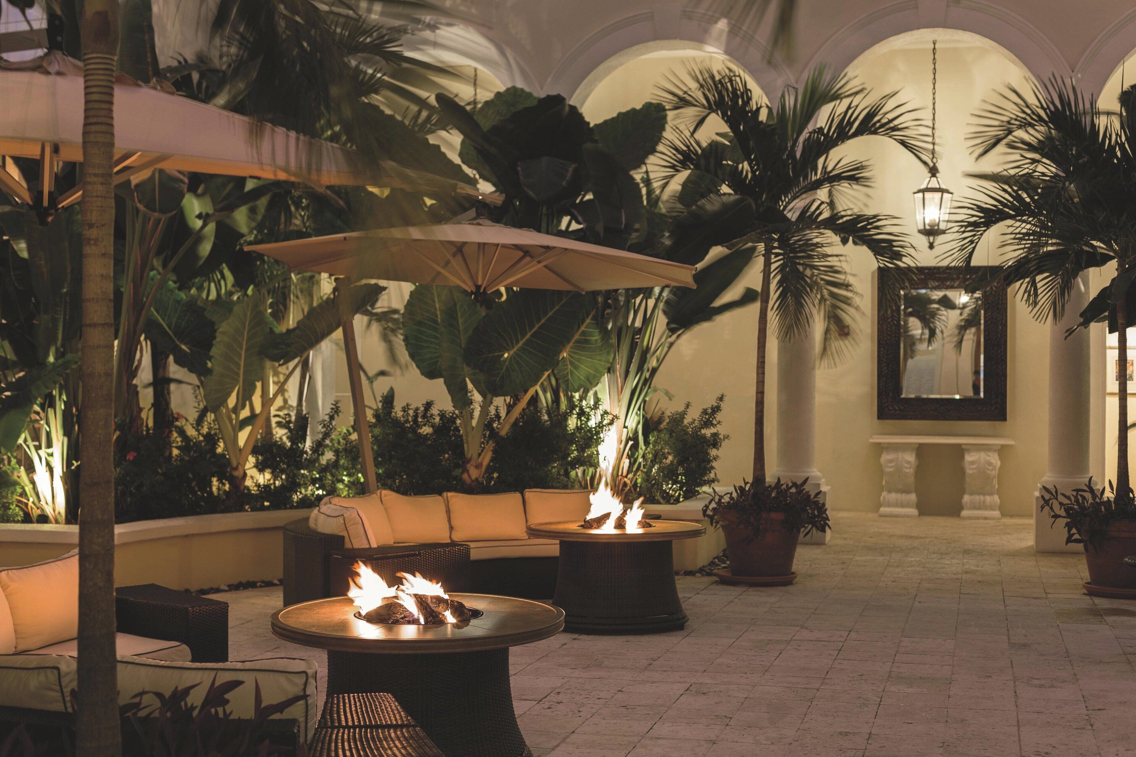 A cozy outdoor seating area with a fire pit, lounge chairs, and potted plants.