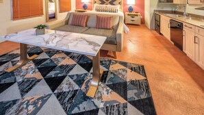 Habitación de hotel compacta con cama, mesa de comedor, sofá, zona de cocina y alfombra estampada.