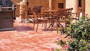 Un patio al aire libre con una parrilla, sillas de madera y una sombrilla.