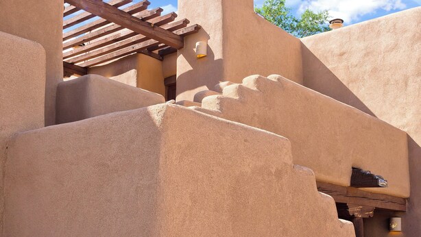 Un edificio con una pérgola de madera y una escalera que sube a un nivel superior.