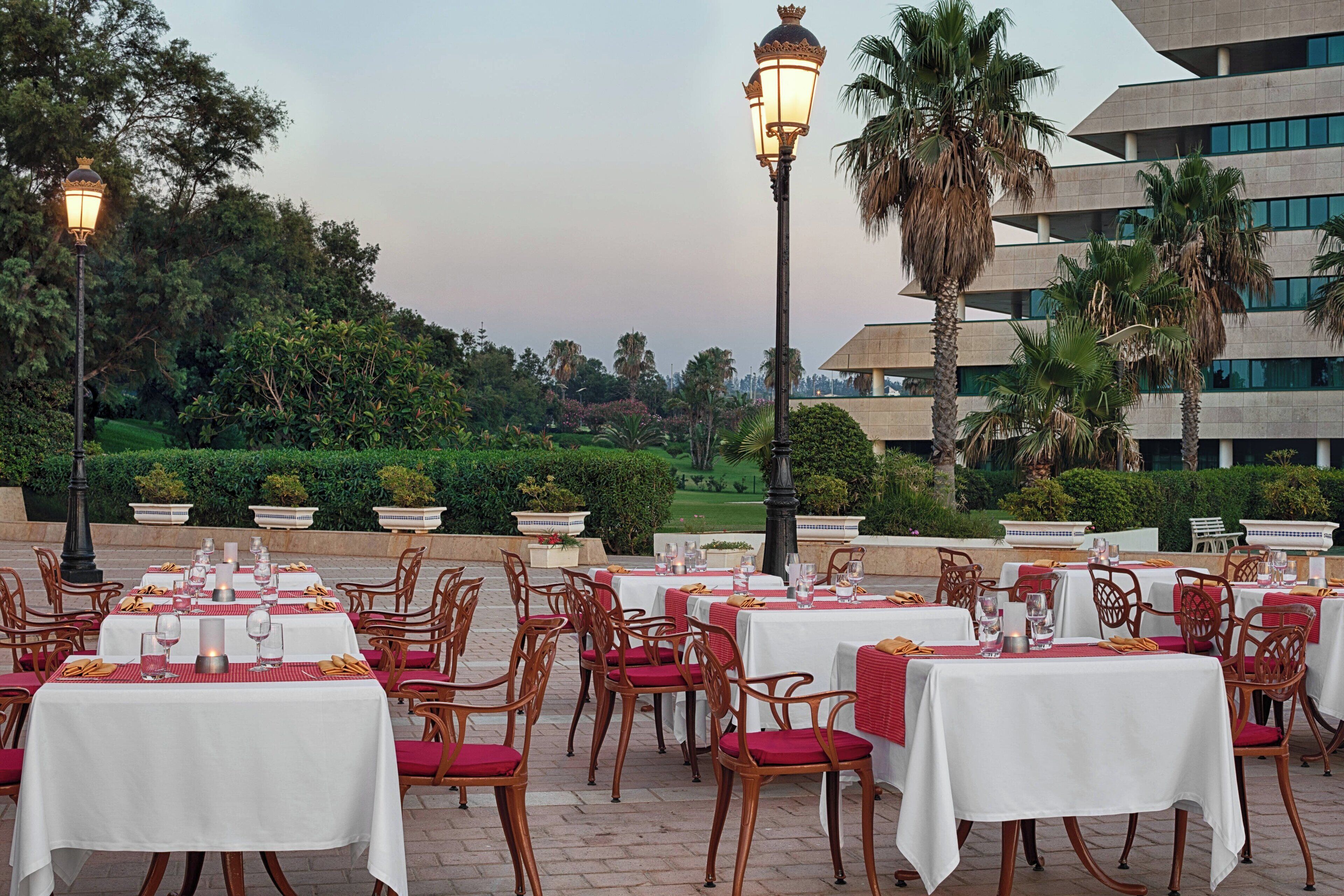 An outdoor dining area with tables set for guests, surrounded by lush greenery and palm trees.