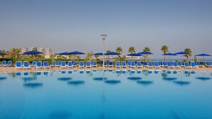 A pool area with blue lounge chairs and umbrellas, a clear sky, and a distant cityscape. - Sheraton Club des Pins Resort (Algiers)
