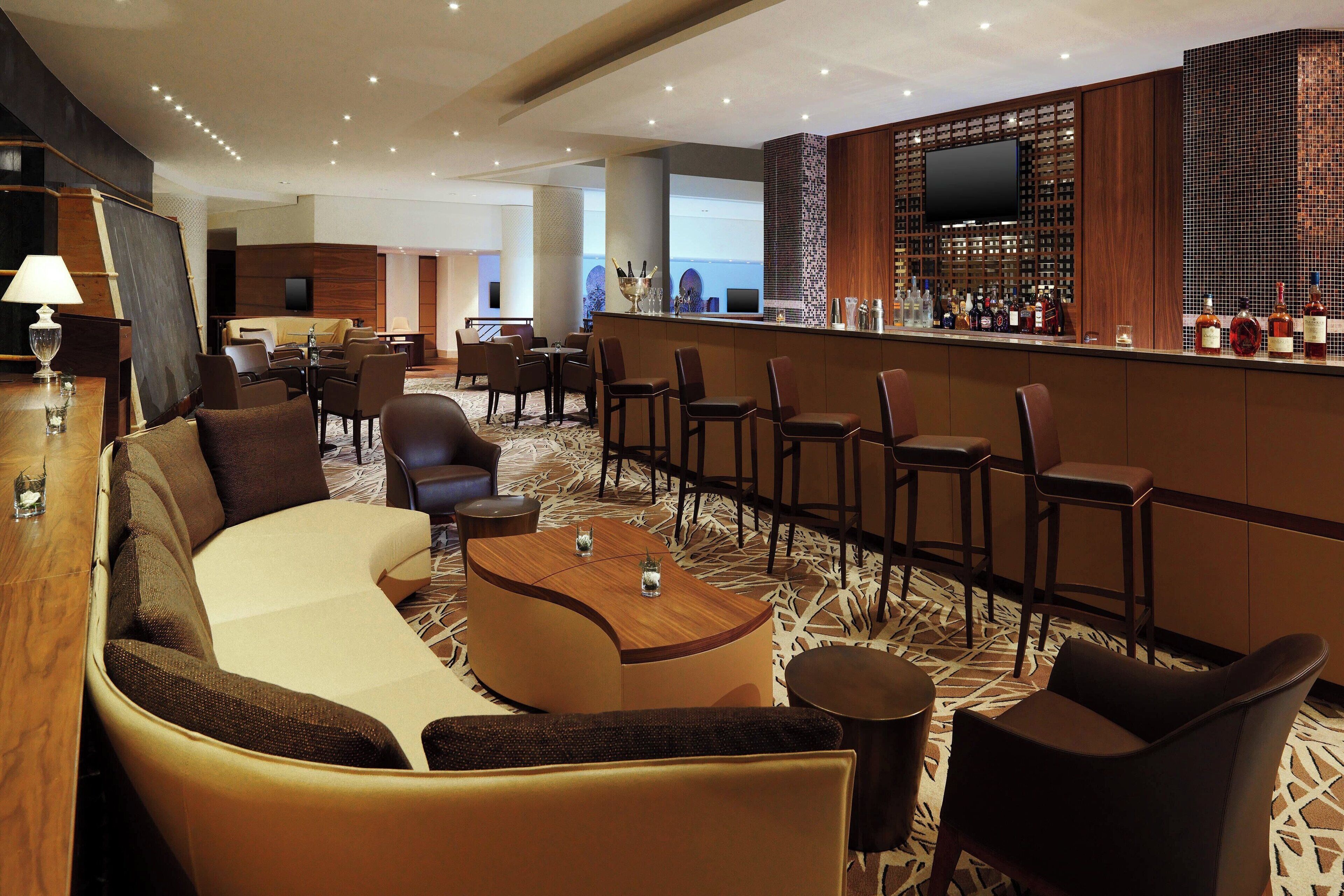 A hotel lobby with a bar area, seating arrangements, and a television screen.