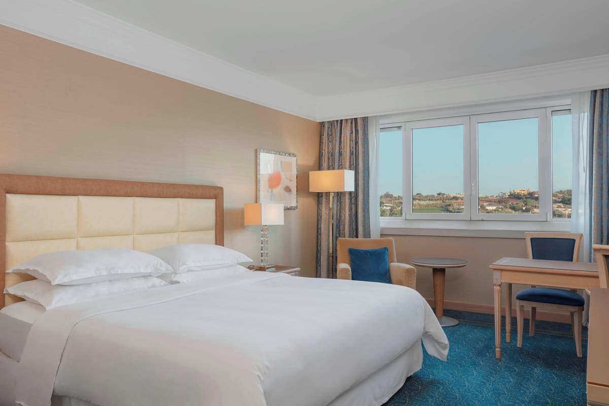 Ein Hotelzimmer mit einem großen Bett, einem Schreibtisch, einem Stuhl und Blick auf die Landschaft durch das Fenster.