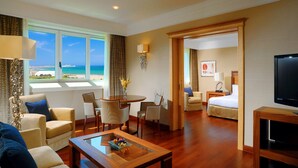 A hotel room with a view of the sea, a dining area, a sitting area with a coffee table, and a bedroom with a bed and a TV. - Sheraton Club des Pins Resort (Algiers)