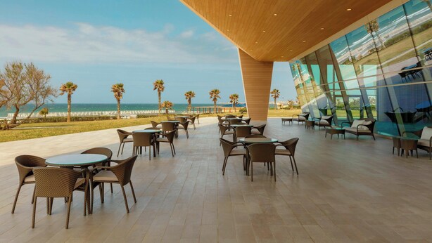 An outdoor seating area with tables and chairs, overlooking a beach and ocean. - Sheraton Club des Pins Resort (Algiers)