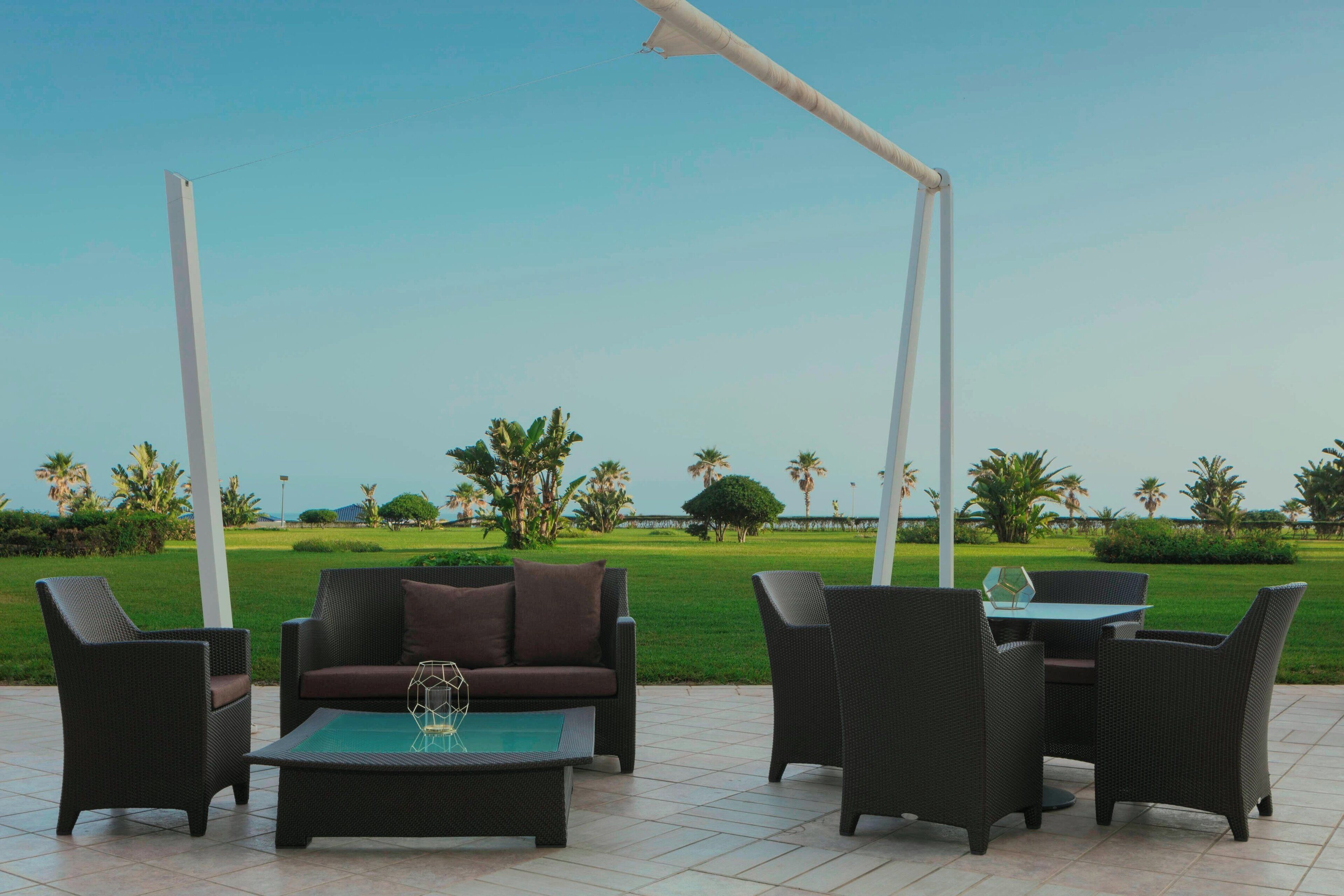 An outdoor seating area with a sofa, chairs, and a table, overlooking a well-maintained lawn and palm trees.