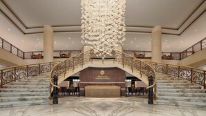 A grand lobby with a marble staircase, a large chandelier, and a reception desk labeled "Sheraton Club Des Pins". - Sheraton Club des Pins Resort (Algiers)