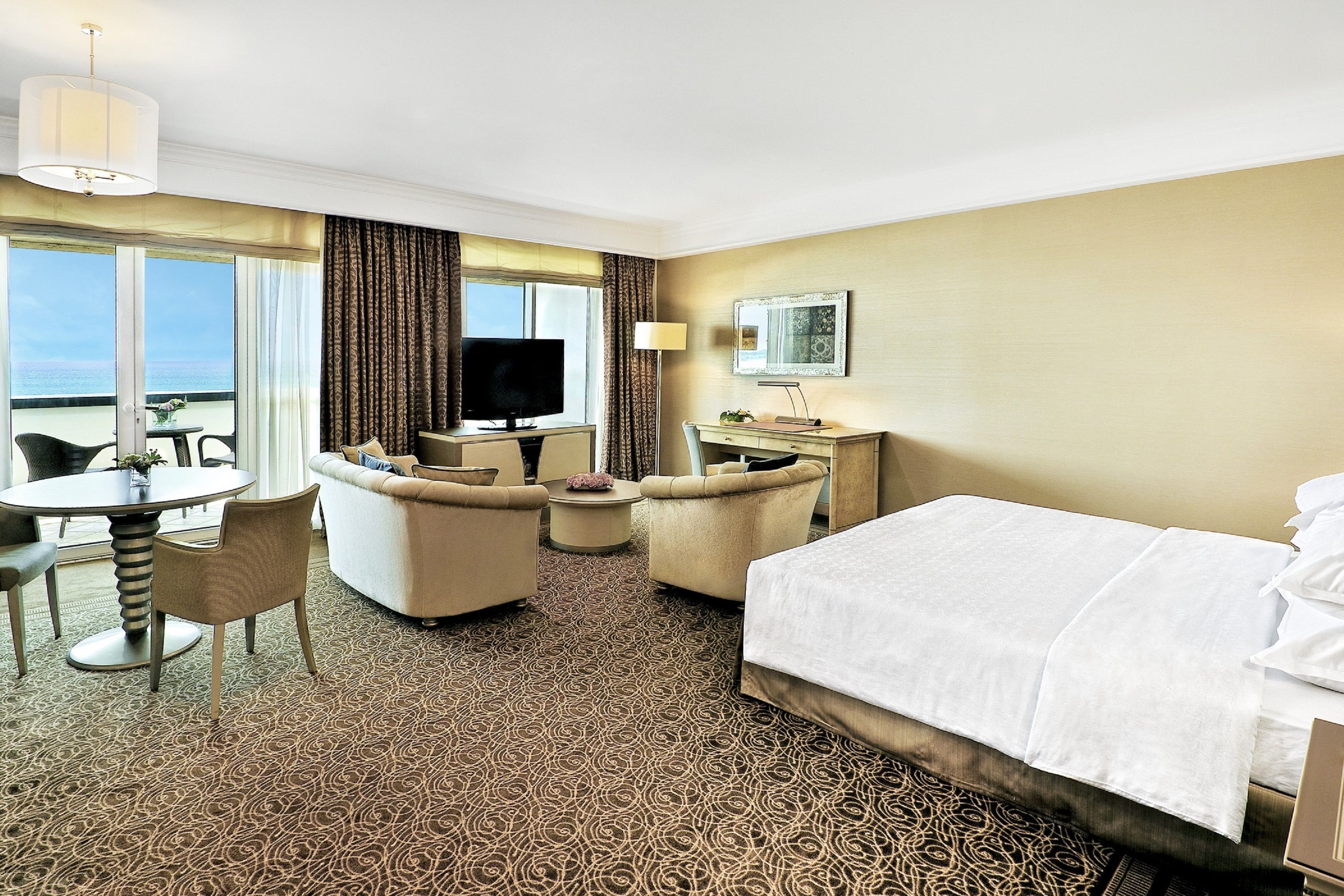 Habitación de hotel con cama, escritorio, silla, televisor y vista al océano.