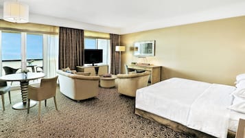 Habitación de hotel con cama, escritorio, silla, televisor y vista al océano.