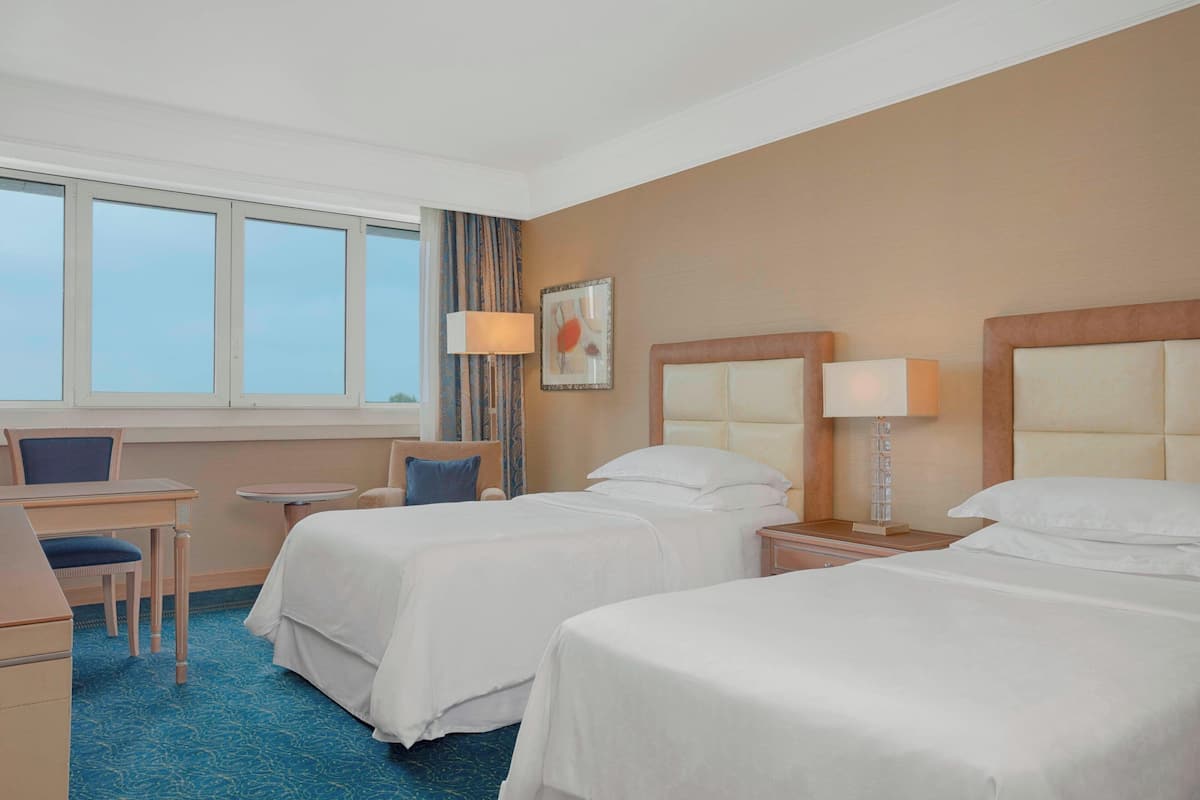 Ein Hotelzimmer mit zwei Betten, einem Schreibtisch, einem Stuhl und einem Vorhangfenster.