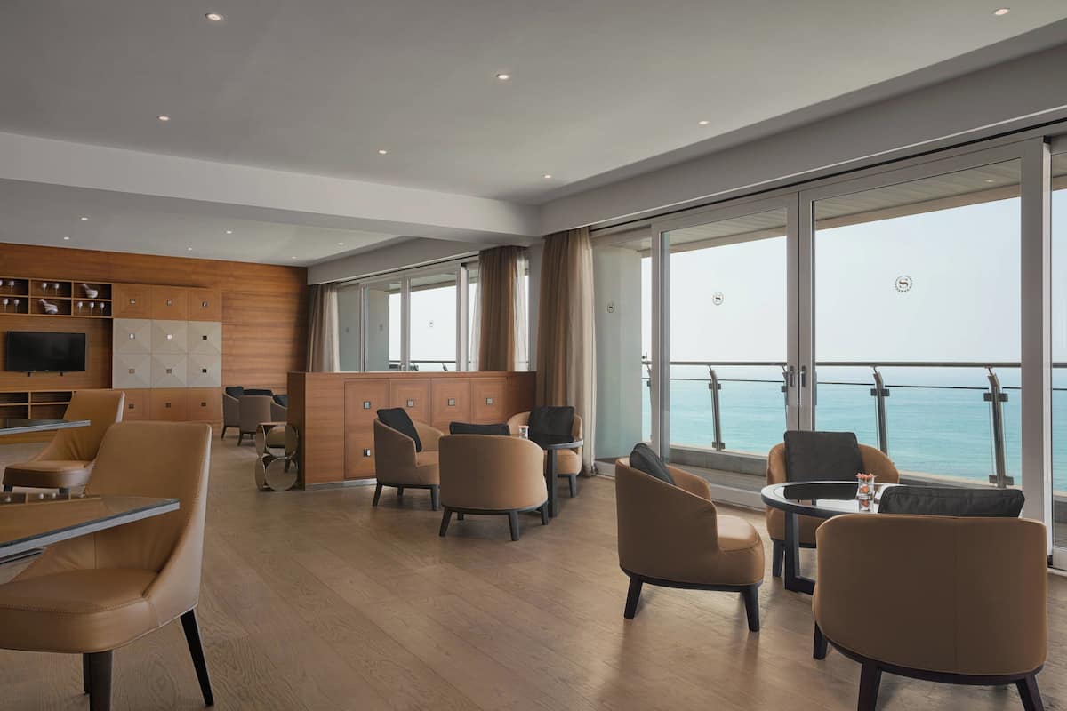 Ein modernes Interieur mit einer Holzwand, einer Bar und Sitzgelegenheiten, die große Fenster mit Meerblick bieten.