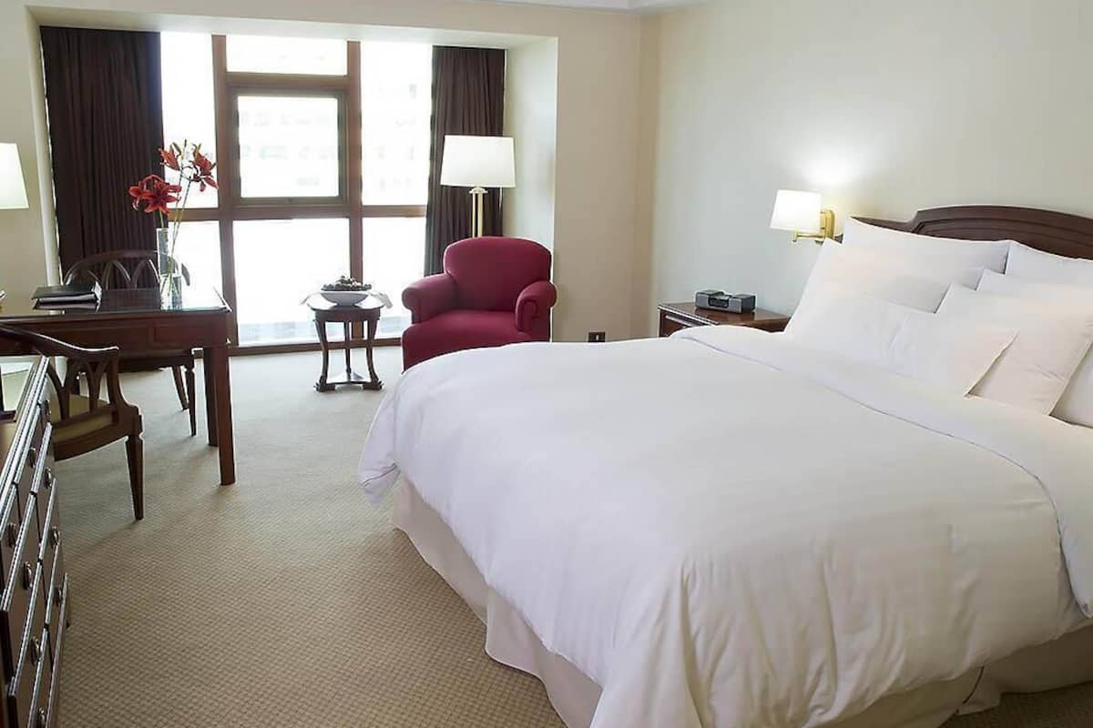 Une chambre d’hôtel avec un grand lit, un bureau, une chaise, une lampe et une fenêtre avec des rideaux.