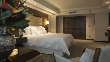 Una habitación de hotel con cama, mesitas de noche, una lámpara, un jarrón con flores y una silla.
