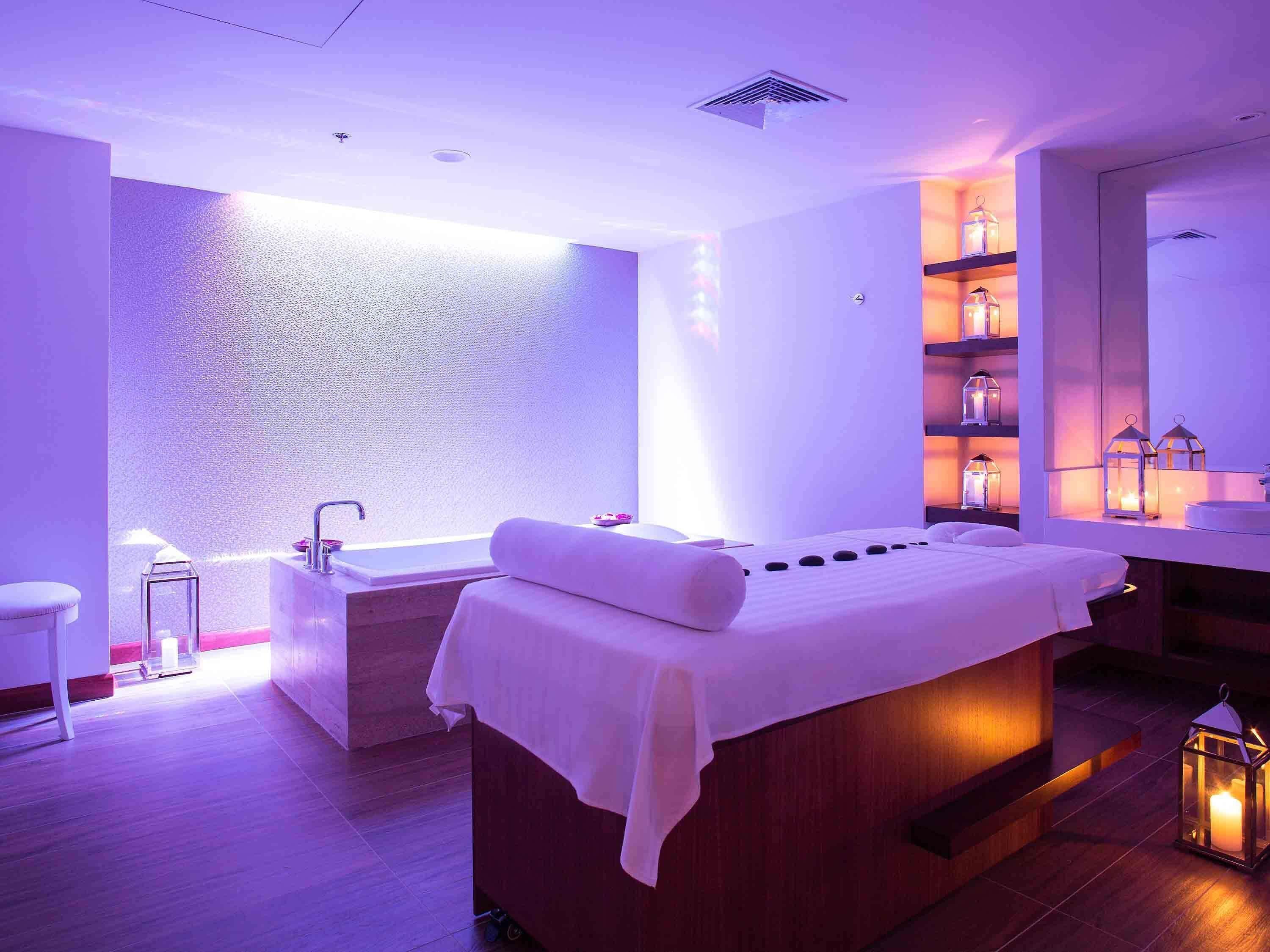 A spa room with a massage table, a bathtub, and a wall with a textured surface.