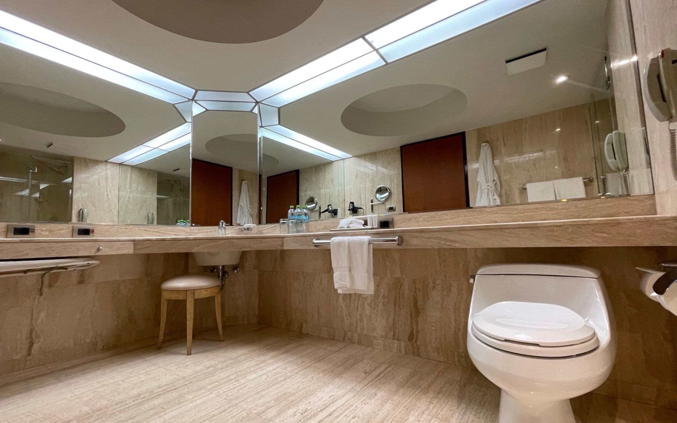 A modern bathroom with a large mirror, a toilet, a sink, and a vanity.