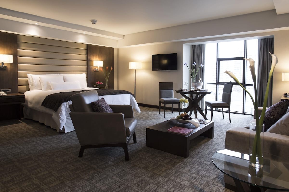 A hotel room with a bed, two armchairs, a coffee table, a TV, and a large window.