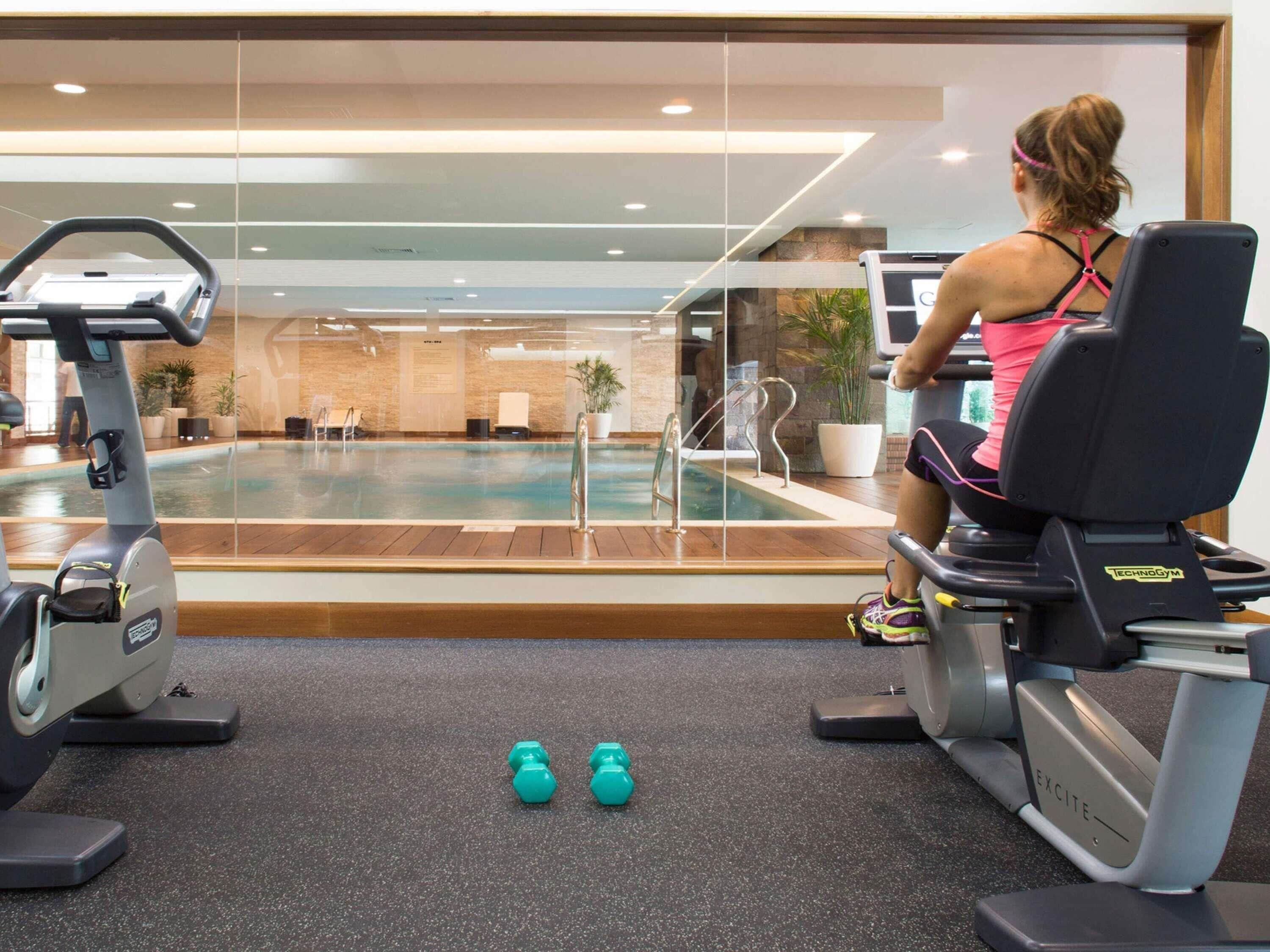 A gym with an indoor pool, exercise equipment, and a woman using a stationary bike.