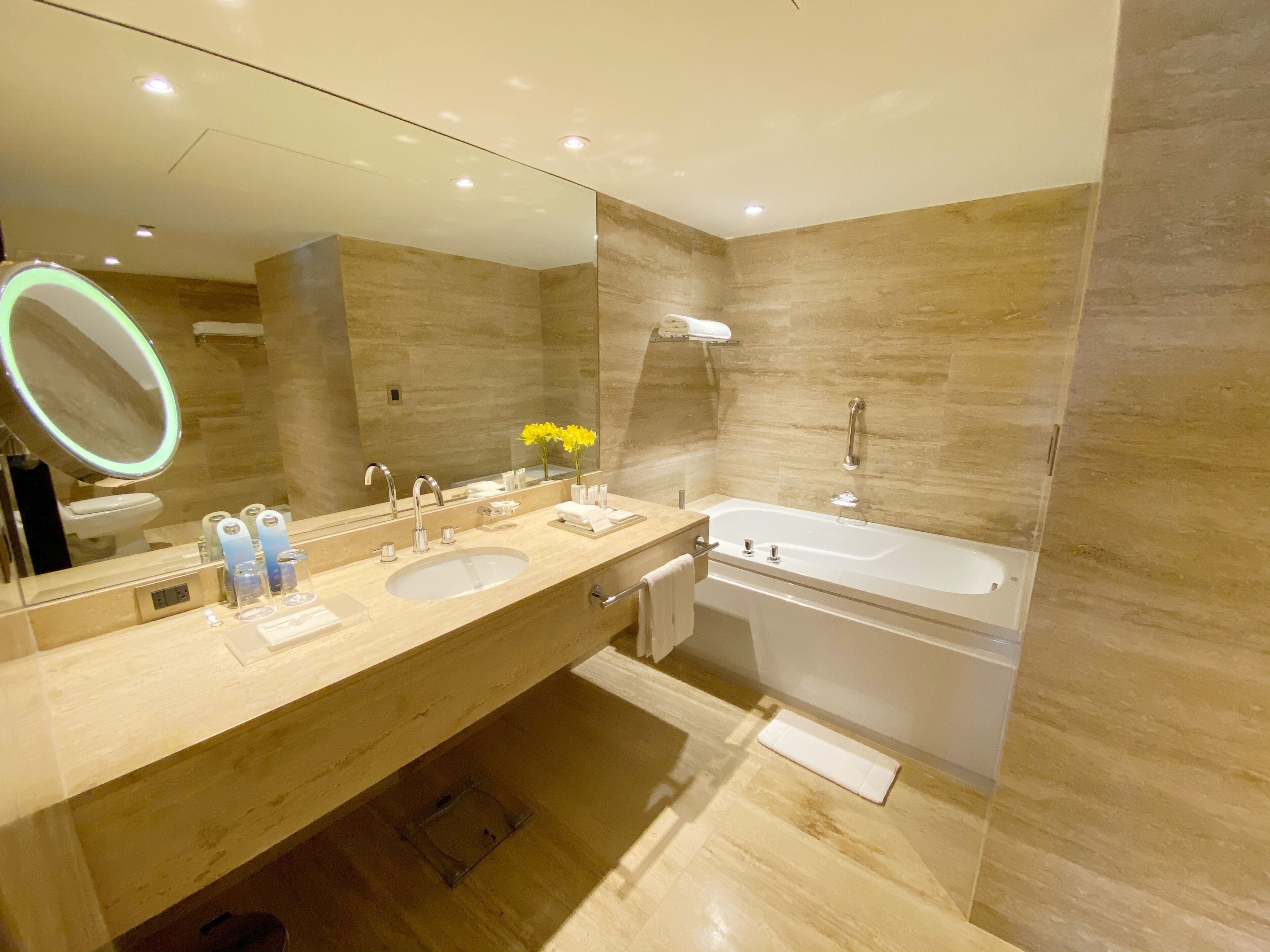 Une salle de bain moderne avec un double vasque, un grand miroir, une baignoire et un meuble-lavabo avec des articles de toilette.