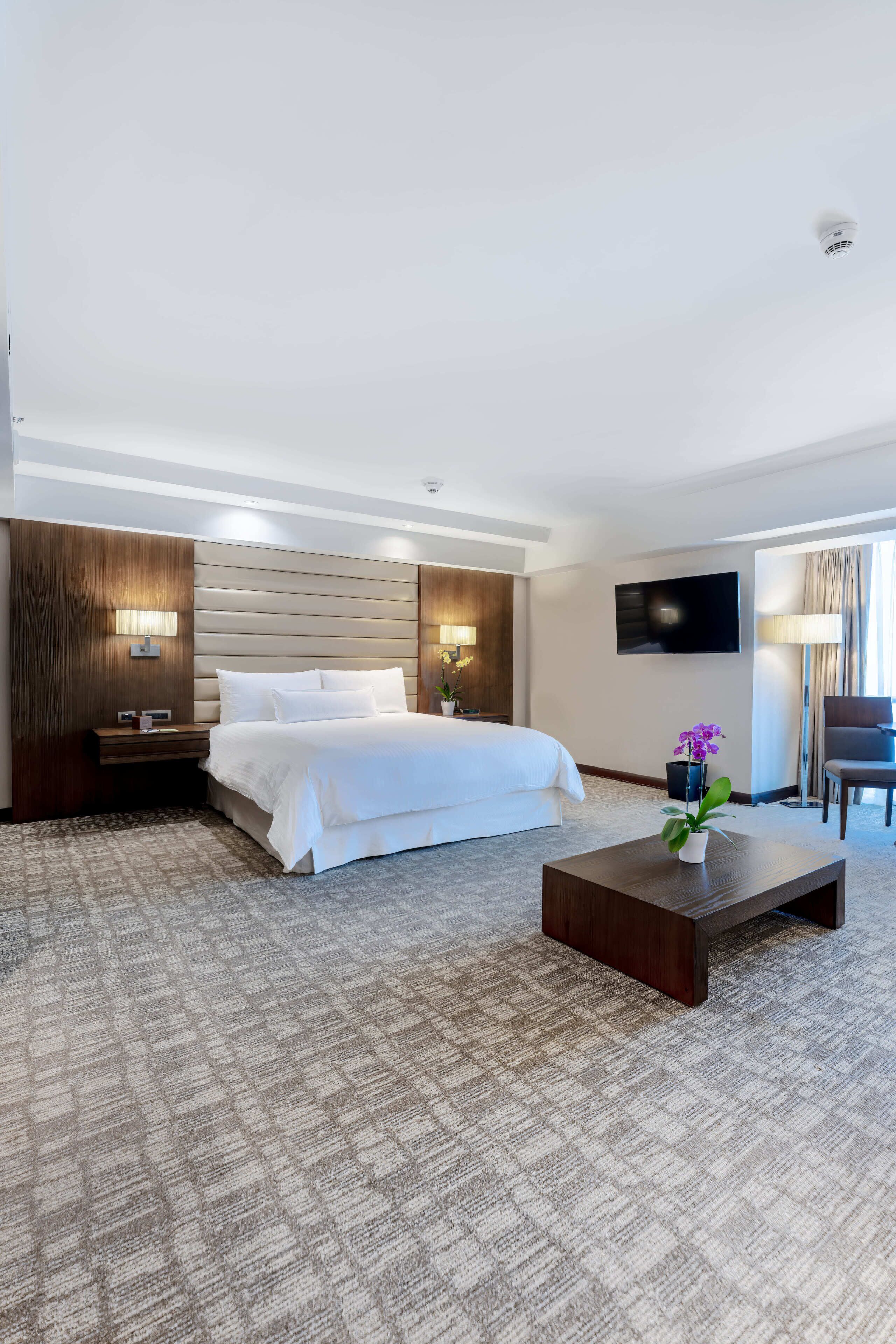 Ein Hotelzimmer mit Bett, Flachbildfernseher, Couchtisch, Lampe und Pflanze.