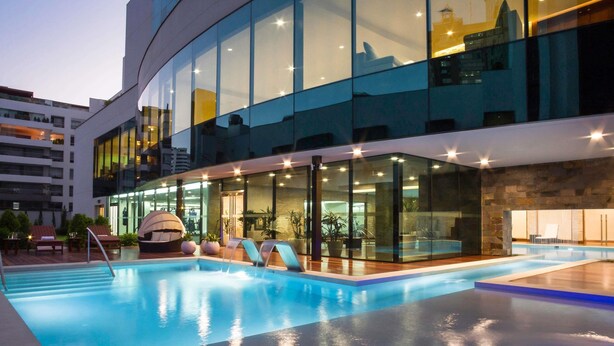 Ett modernt hotell med en swimmingpool, solstolar och ett poolområde som är inbyggt i glas.