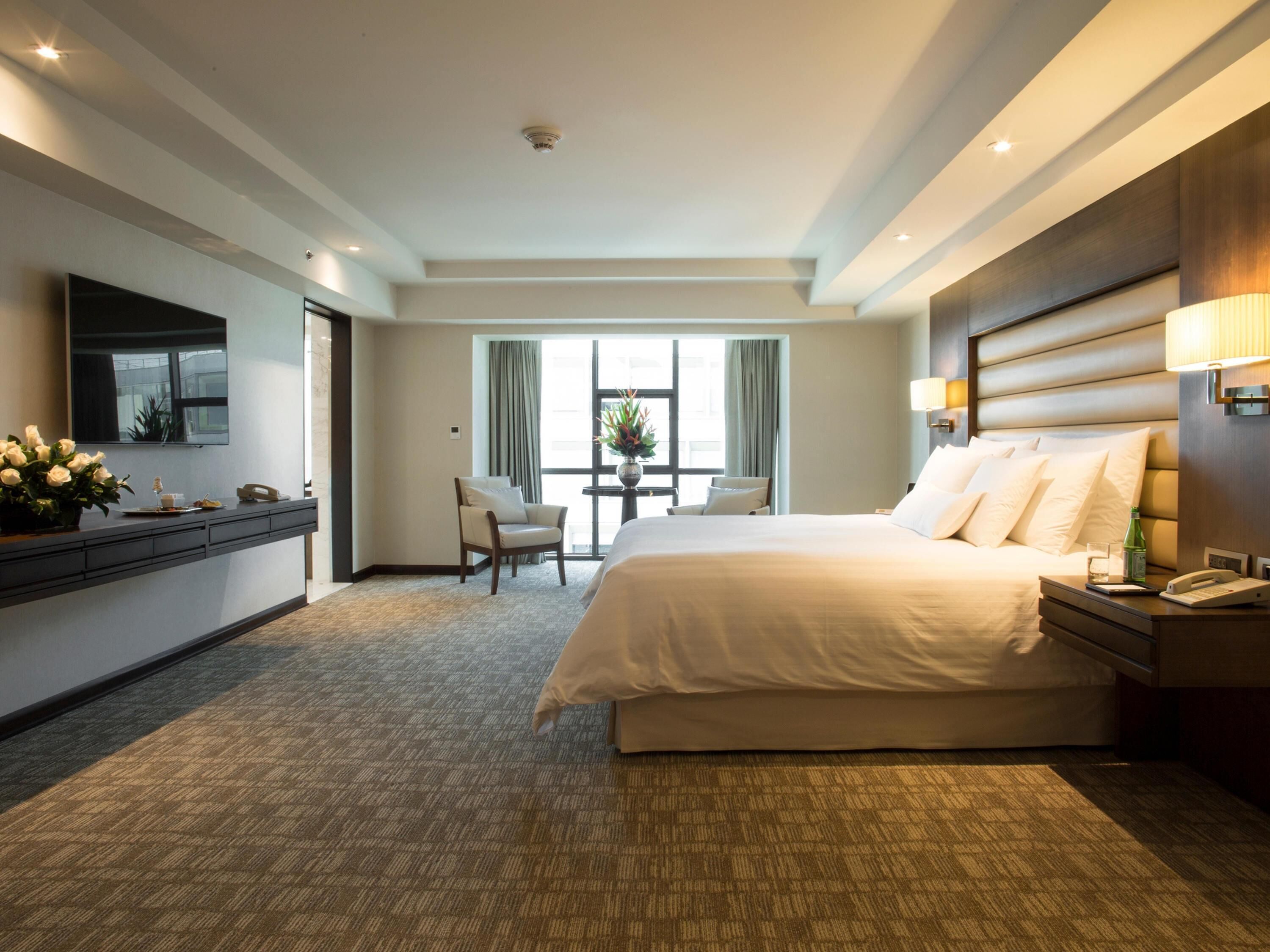 Une chambre d’hôtel avec un grand lit, un bureau avec un téléphone, une chaise et une fenêtre avec des rideaux.