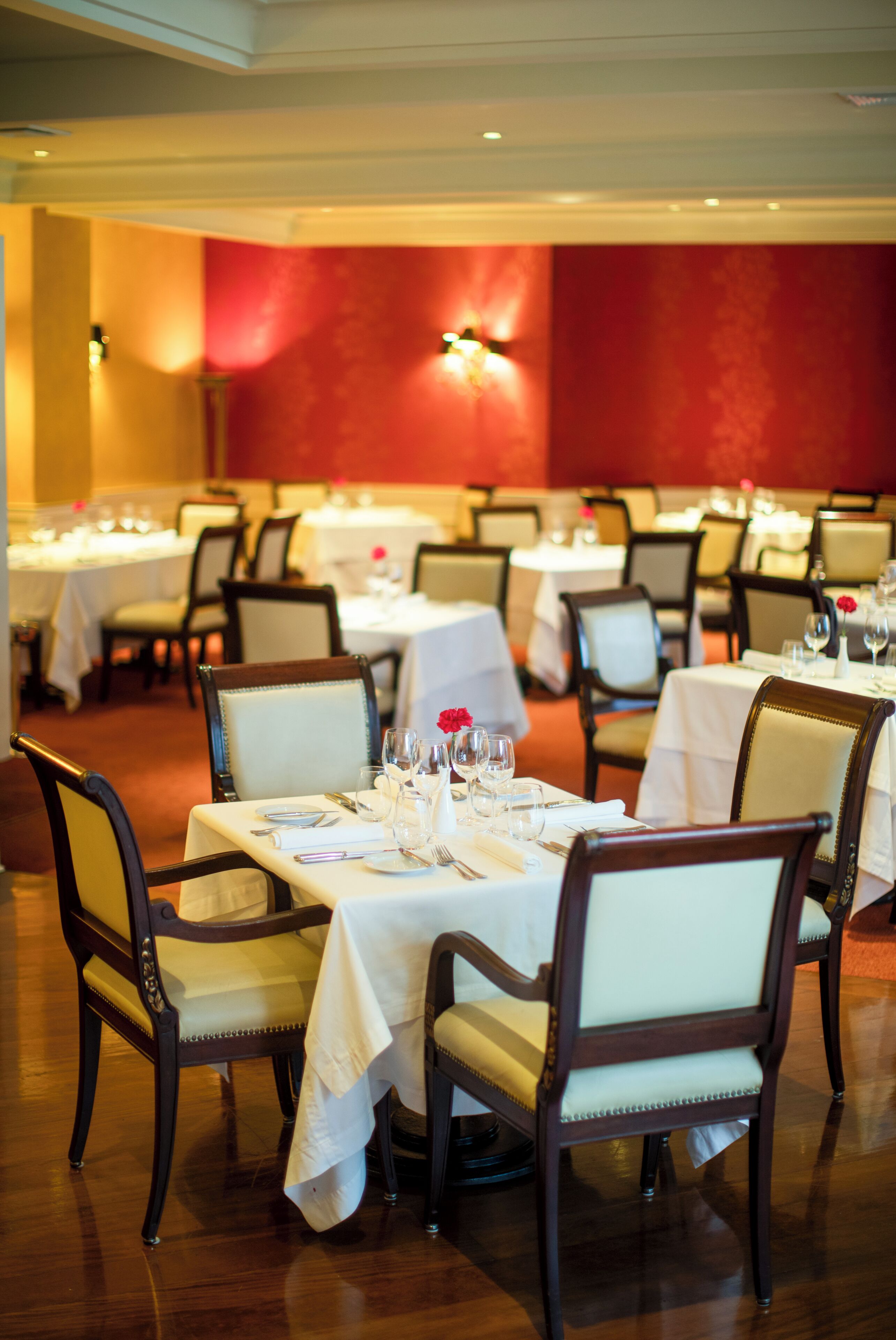 A dining area with multiple tables set for service, chairs, and a red wall in the background.