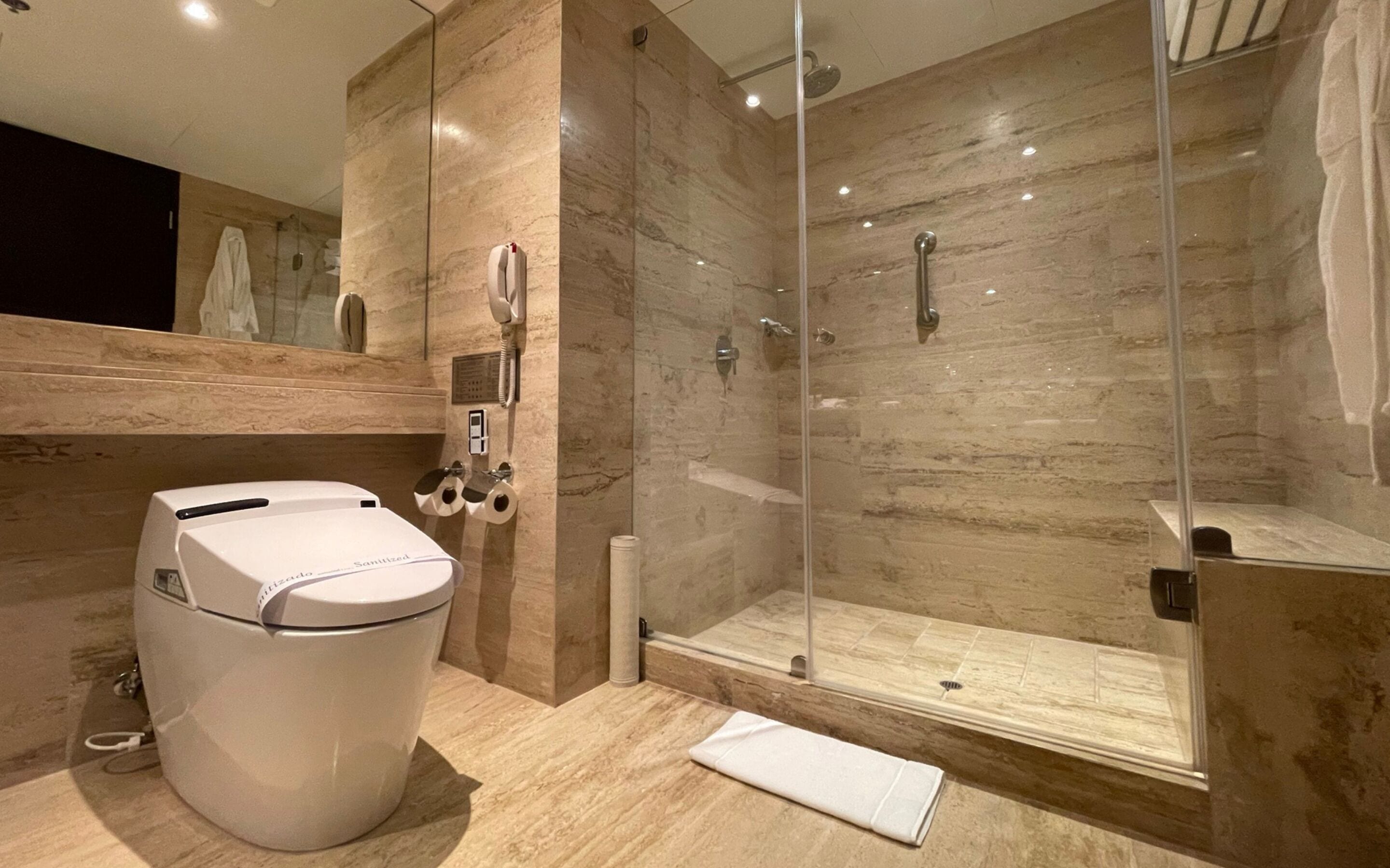 Une salle de bain moderne dotée d’une douche à parois de verre, de toilettes équipées d’un siège bidet et d’un mur recouvert de carreaux de marbre.