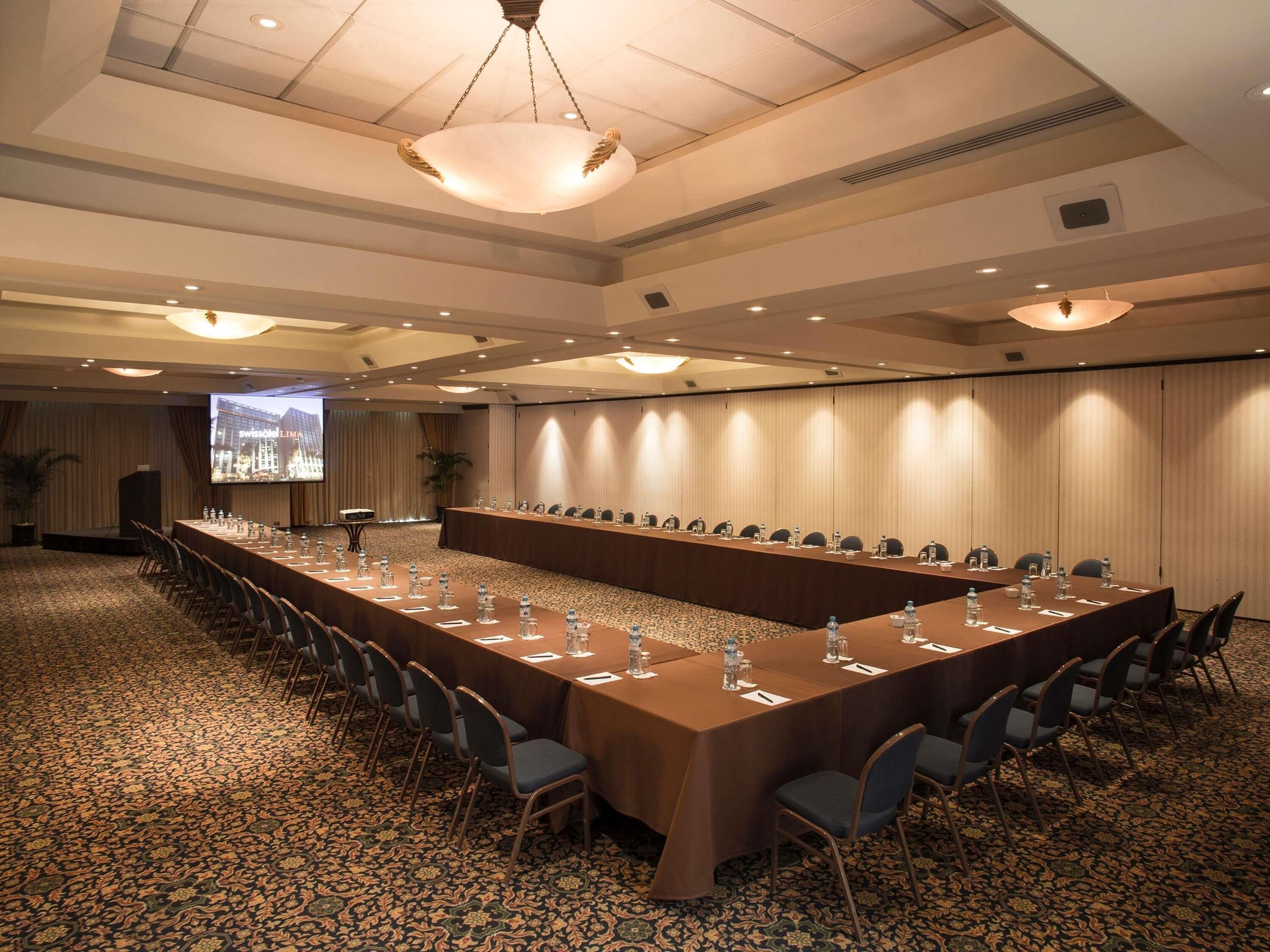 Un salón de conferencias con una larga mesa, sillas y una pantalla para proyector.