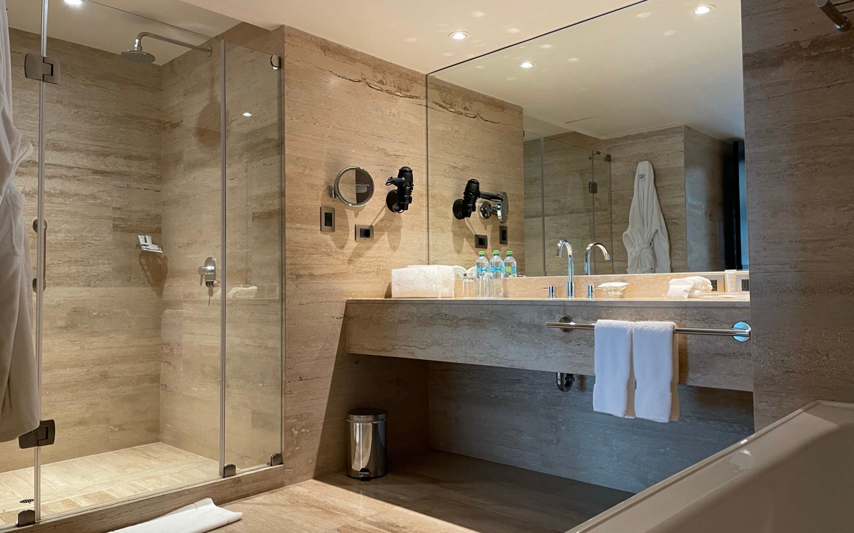 A modern bathroom with a glass-enclosed shower, a vanity with a large mirror, and a towel rack.