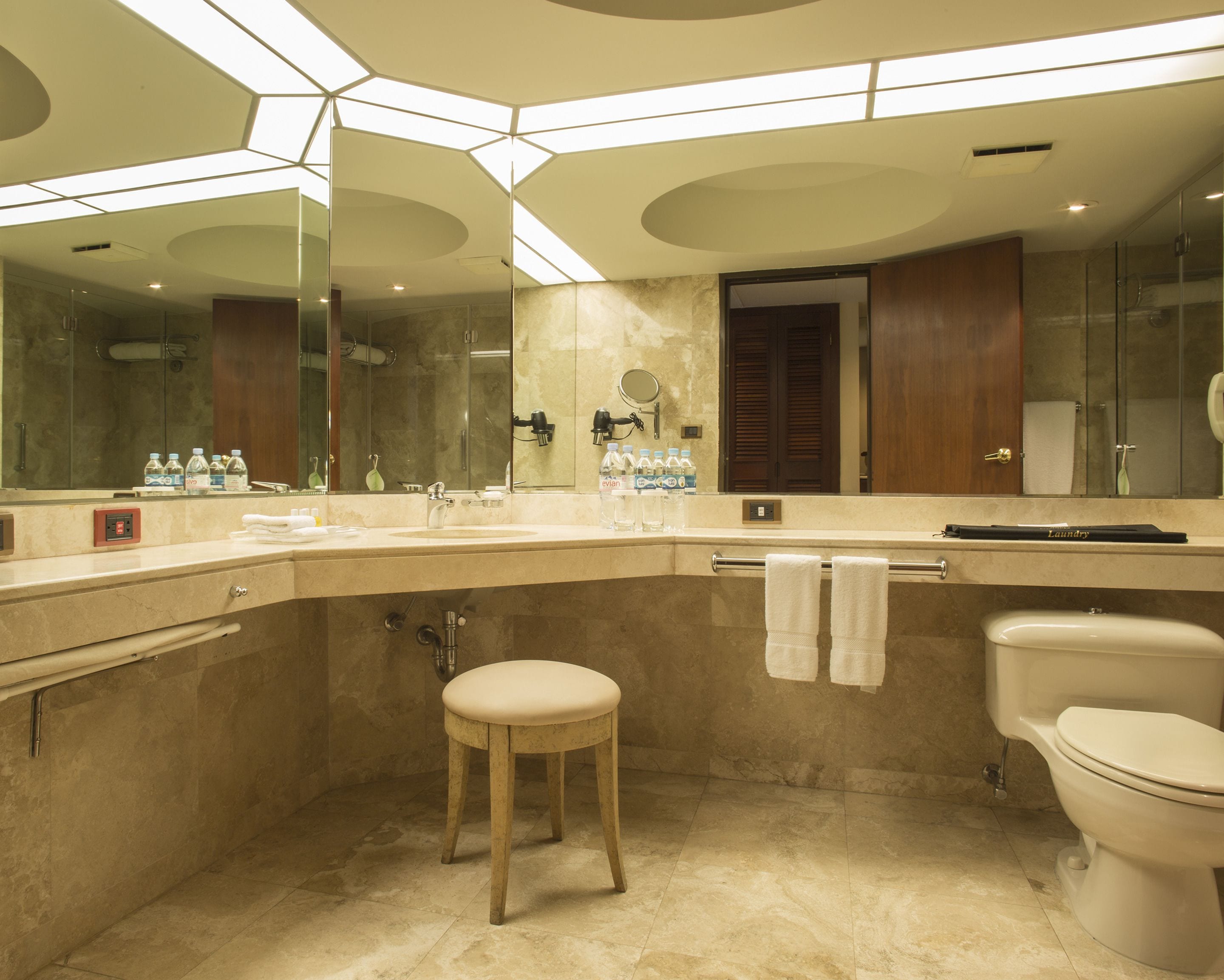 A modern bathroom with a large mirror, a sink, a toilet, and a stool.