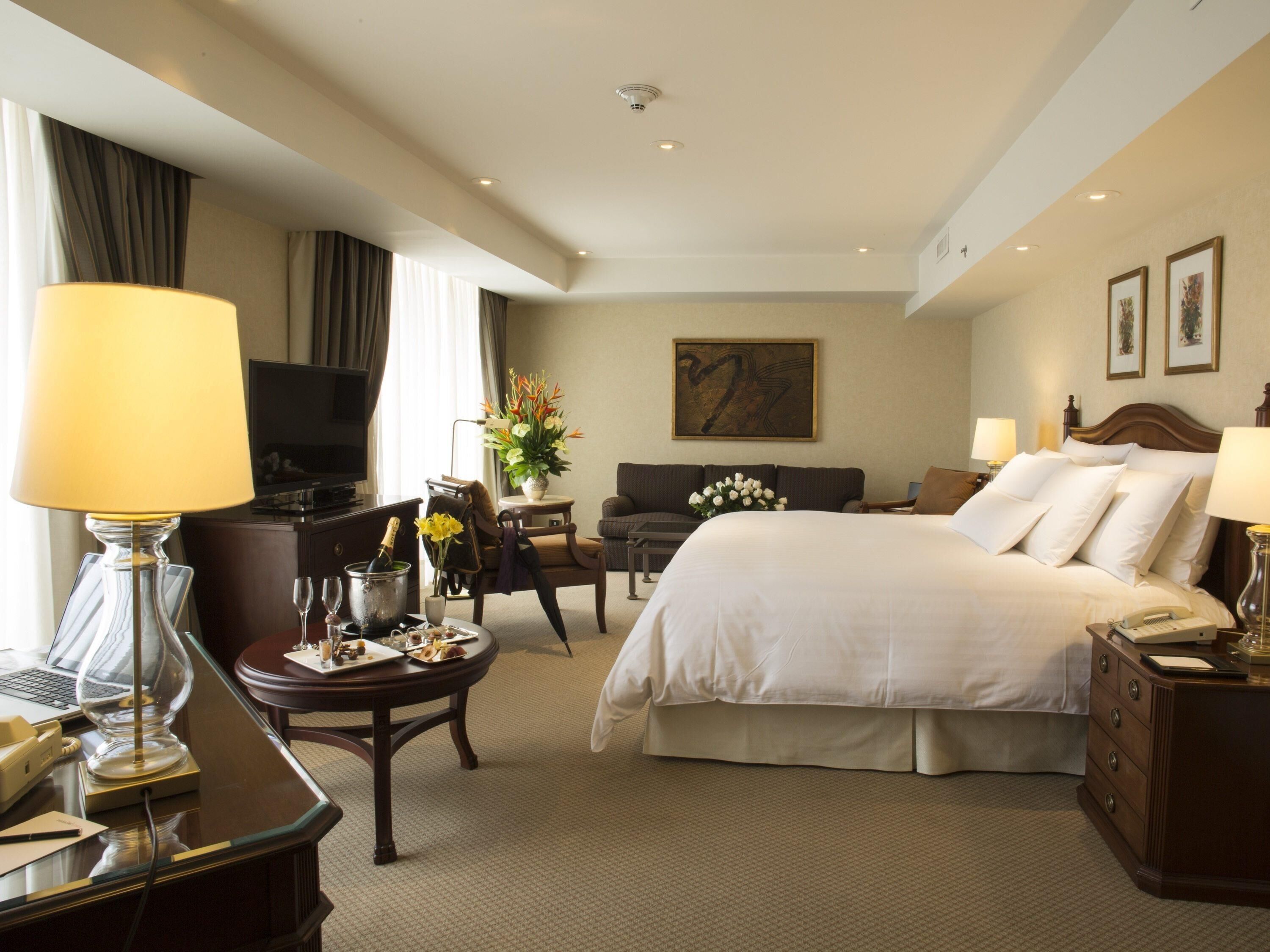 A hotel room with a bed, a desk, a television, a chair, a coffee table, and a painting on the wall.