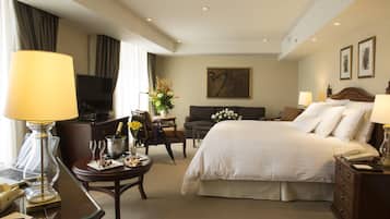 Une chambre d’hôtel avec un lit, un bureau, une télévision, une chaise, une table basse et un tableau au mur.