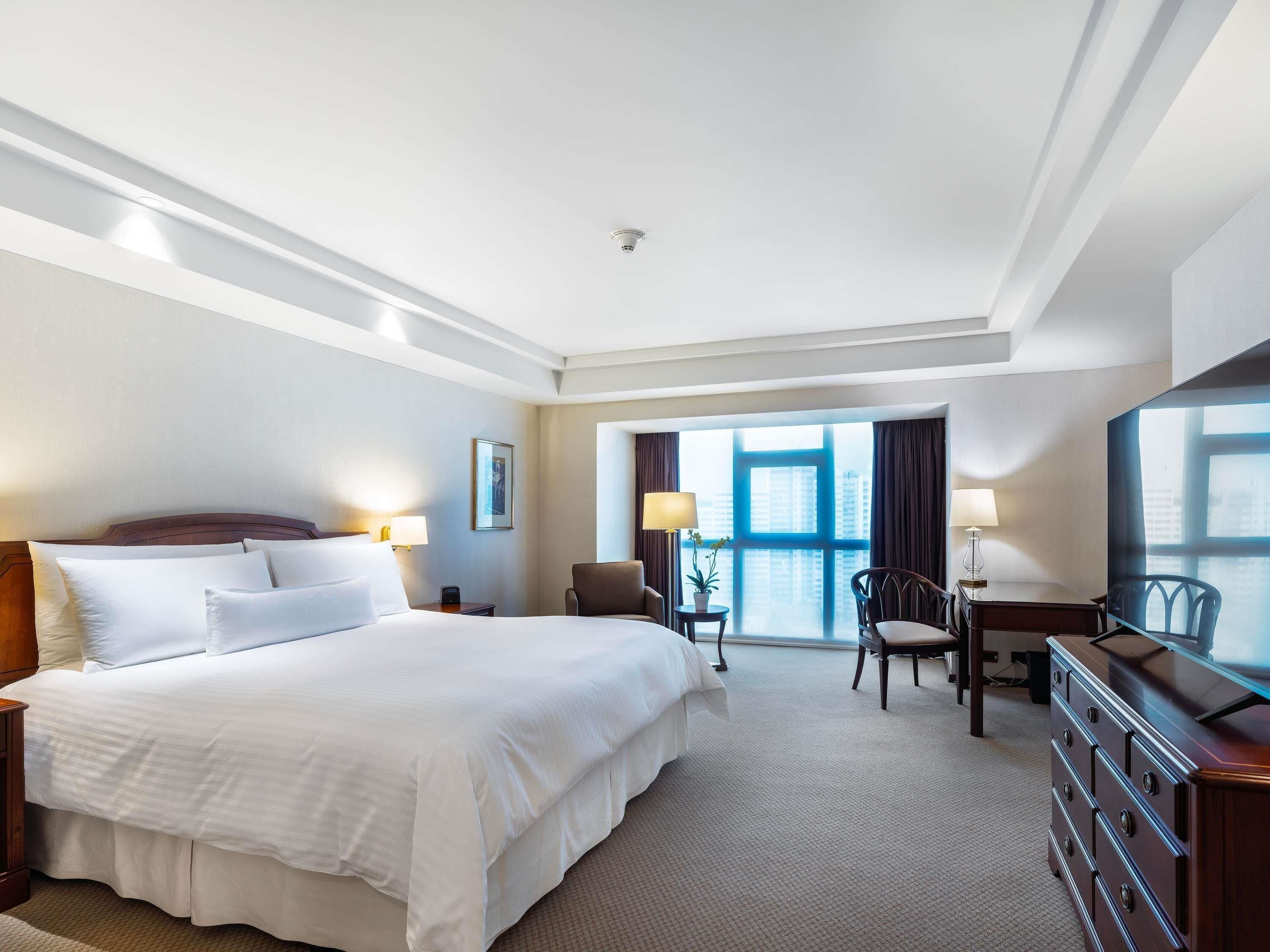Une chambre d’hôtel équipée d’un lit, d’un bureau, d’une chaise, d’une commode et d’une grande fenêtre.