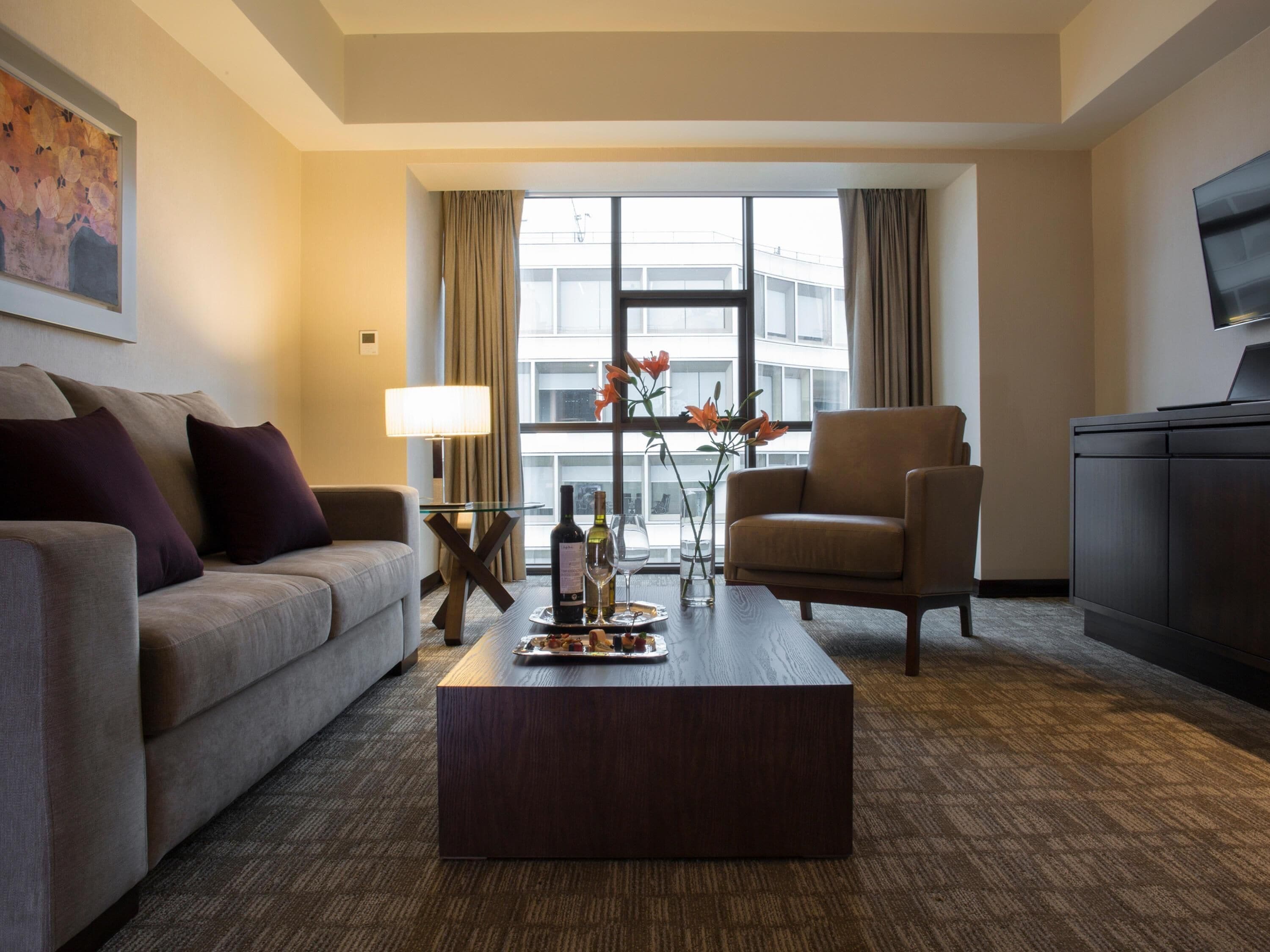 Ein modernes Hotelzimmer mit Sofa, Sesseln, Couchtisch und Fernseher auf einem Schrank.