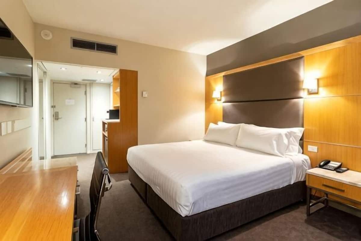 A hotel room with a large bed, bedside table, and a desk with a chair.