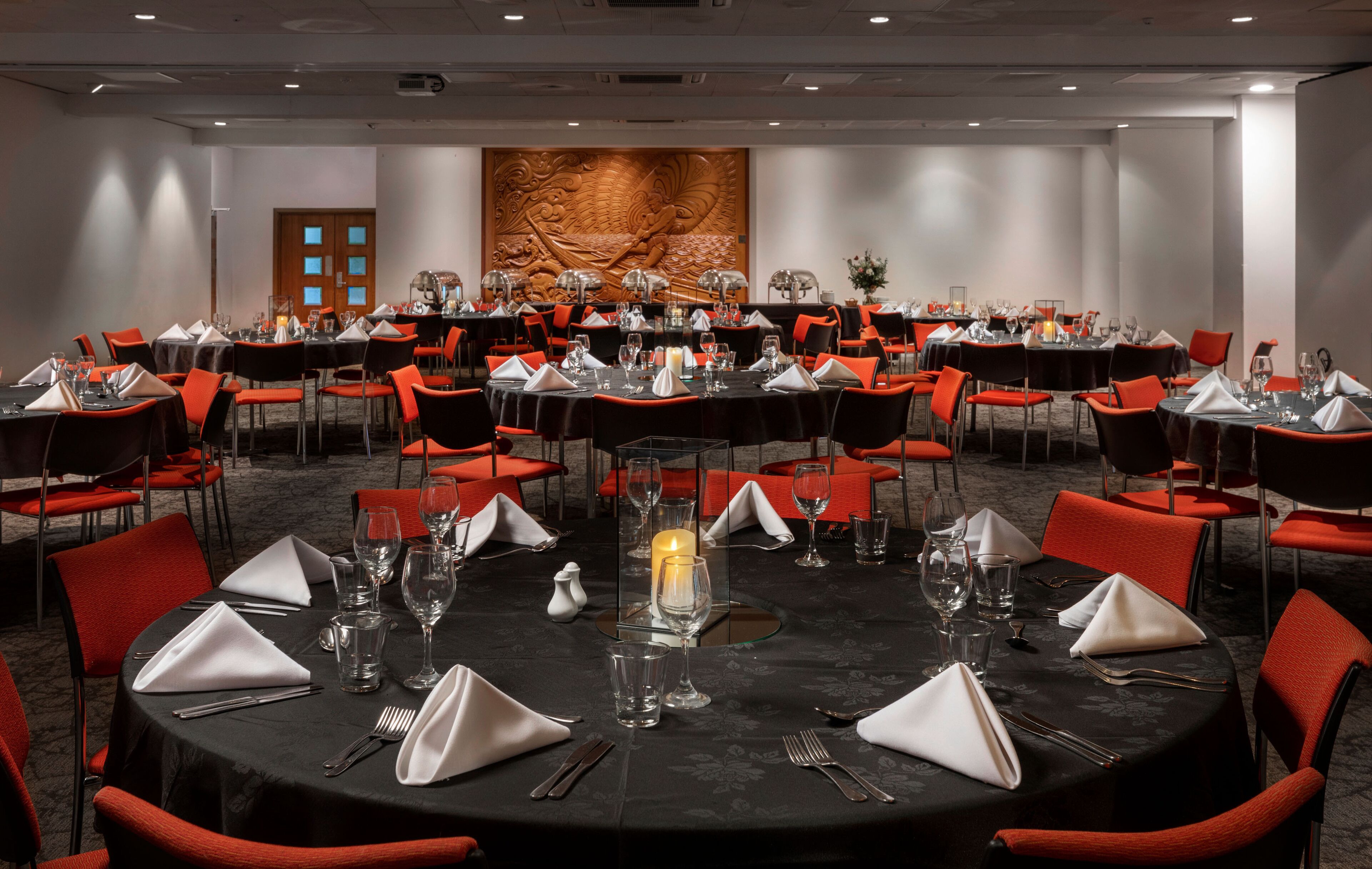 A conference room with round tables, red chairs, and a large decorative wall.