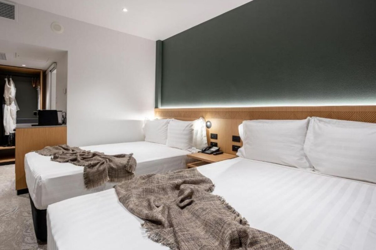 A hotel room with two beds, a wardrobe, a mirror, and a wall-mounted light fixture.