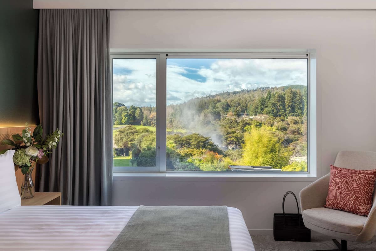 A hotel room with a large window offering a view of a forested landscape.