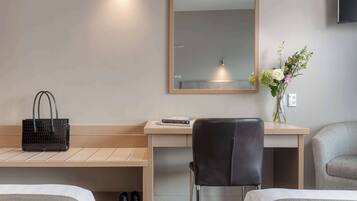 A hotel room with a bed, a desk with a chair, a mirror, a vase with flowers, and a handbag on the desk.