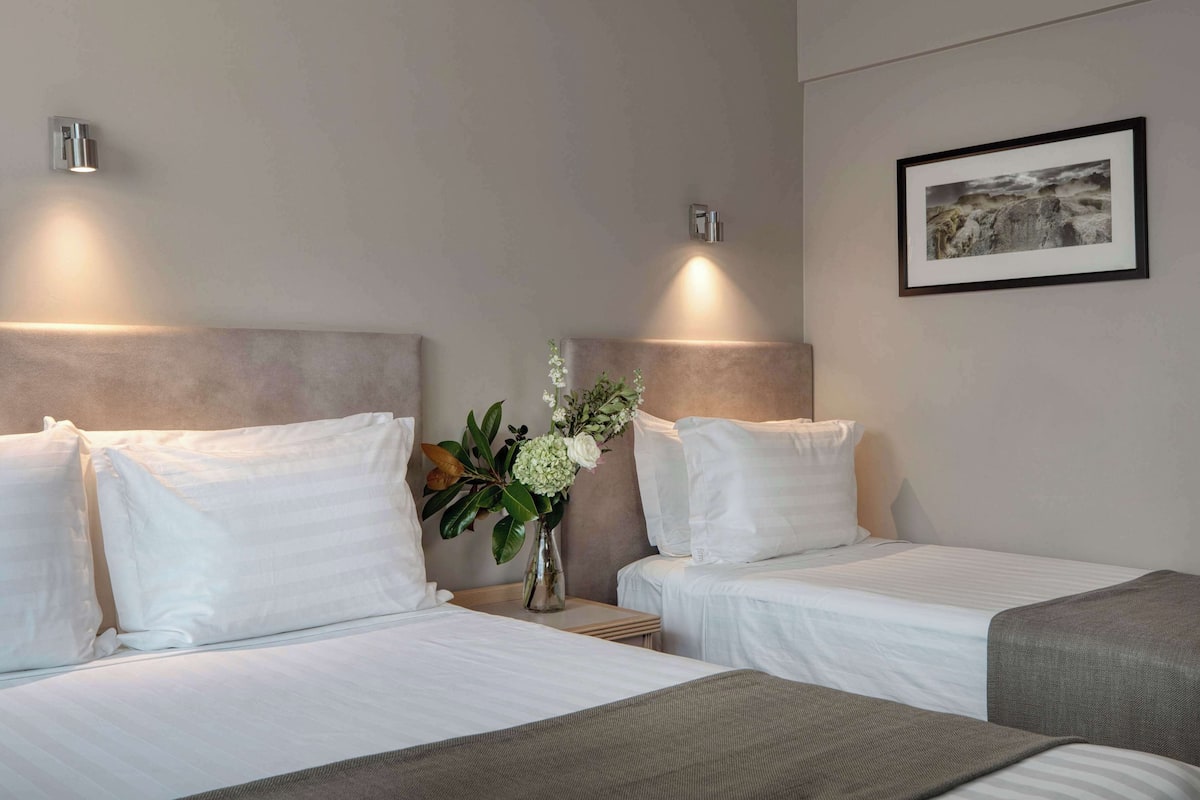 A hotel room with two beds, a nightstand with a vase of flowers, and a framed picture on the wall.