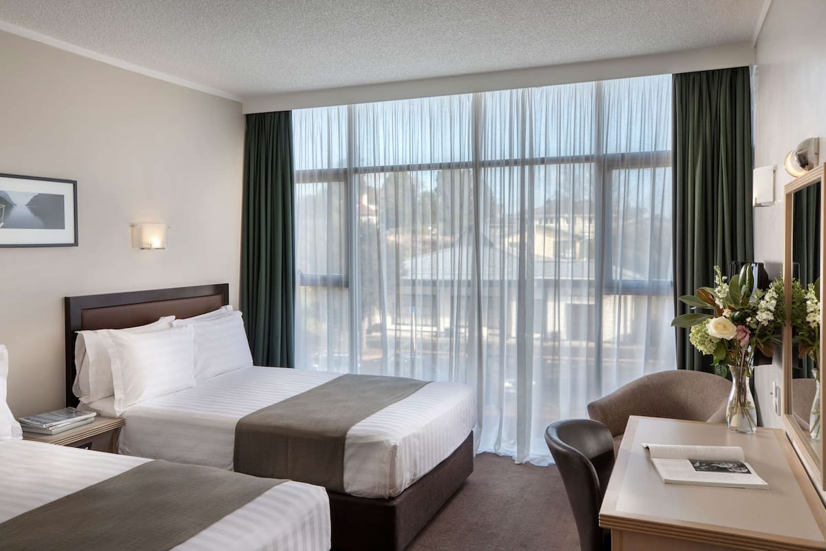 A hotel room with two beds, a desk, a chair, a mirror, and a window with curtains.