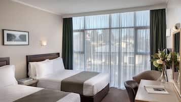 Hotelkamer met twee bedden, een bureau, een stoel, een spiegel en een raam met gordijnen.
