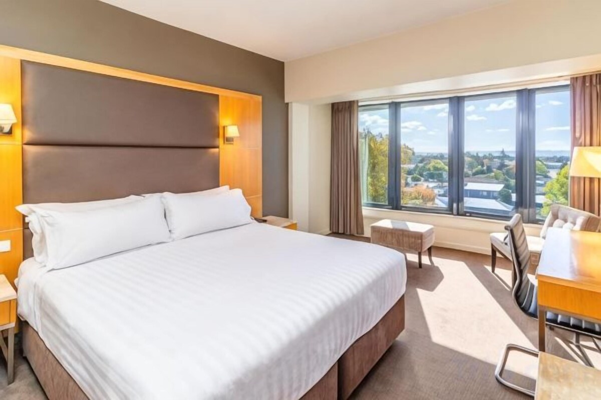 A hotel room with a large bed, a desk, and a view of the city.