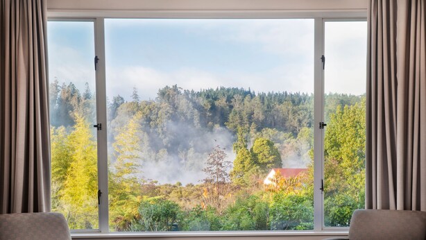 A hotel room with a large window offering a view of a forested area and a house. - Rydges Rotorua (Rotorua)