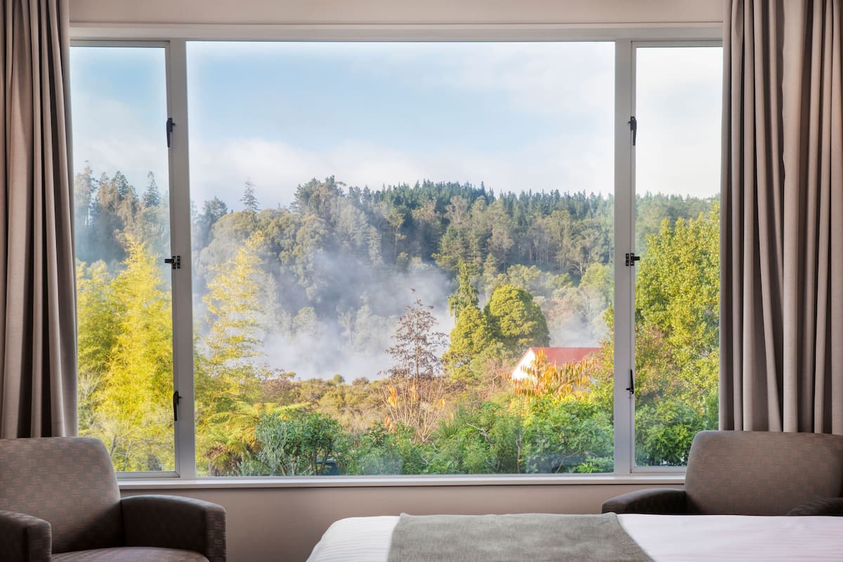 A hotel room with a large window offering a view of a forested area and a house.