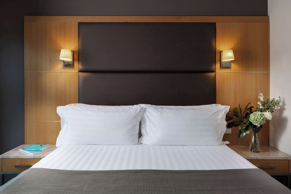 A neatly made bed with white linens, a dark headboard, and two wall-mounted lamps on either side.