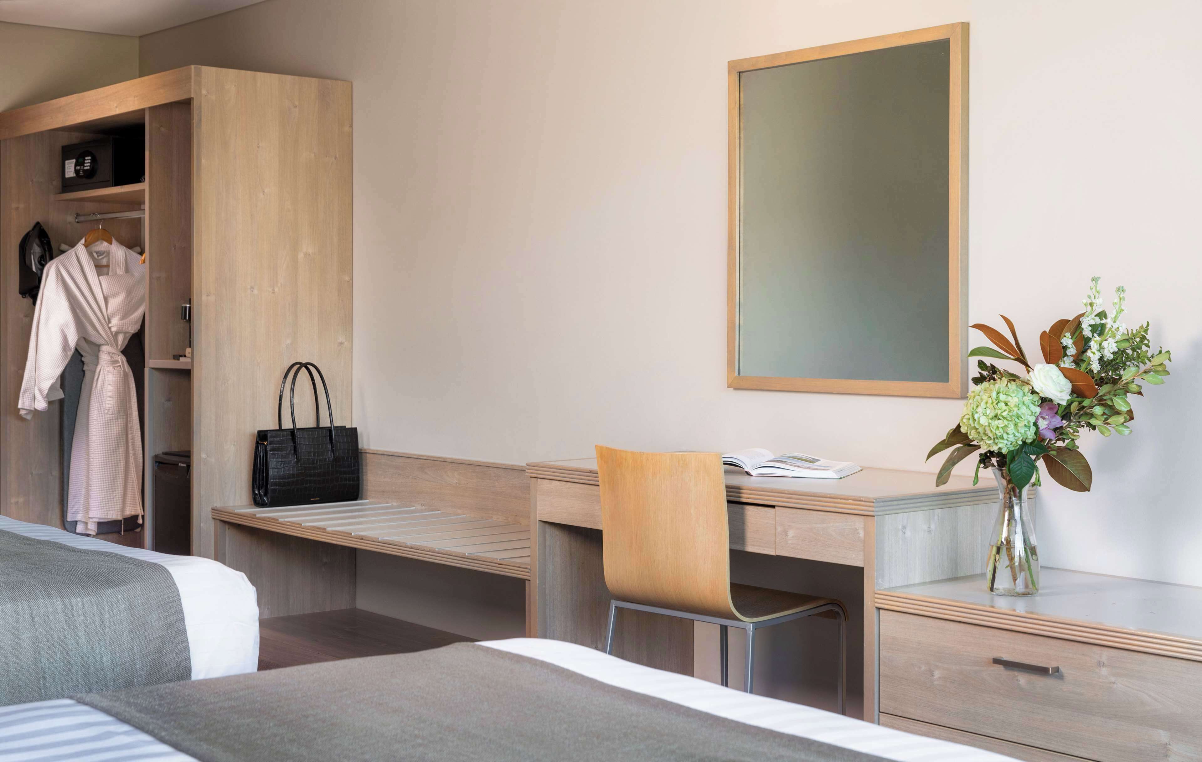 A hotel room with a bed, a desk, a chair, a wardrobe, and a mirror.